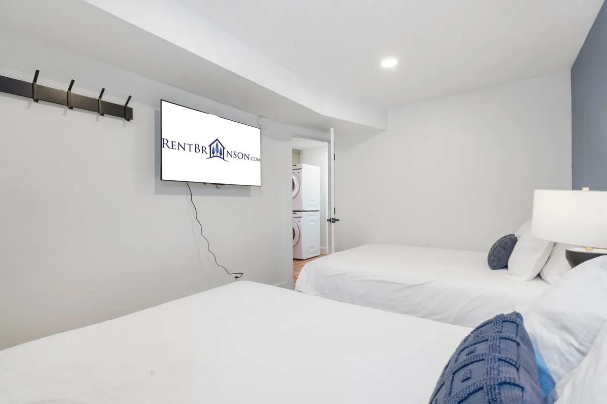 A spacious bedroom setup with two beds, a wall-mounted television, and a functional laundry area. The room is designed for comfort and flexibility, perfect for families or friends traveling together. Soft lighting and modern decor create a welcoming environment.