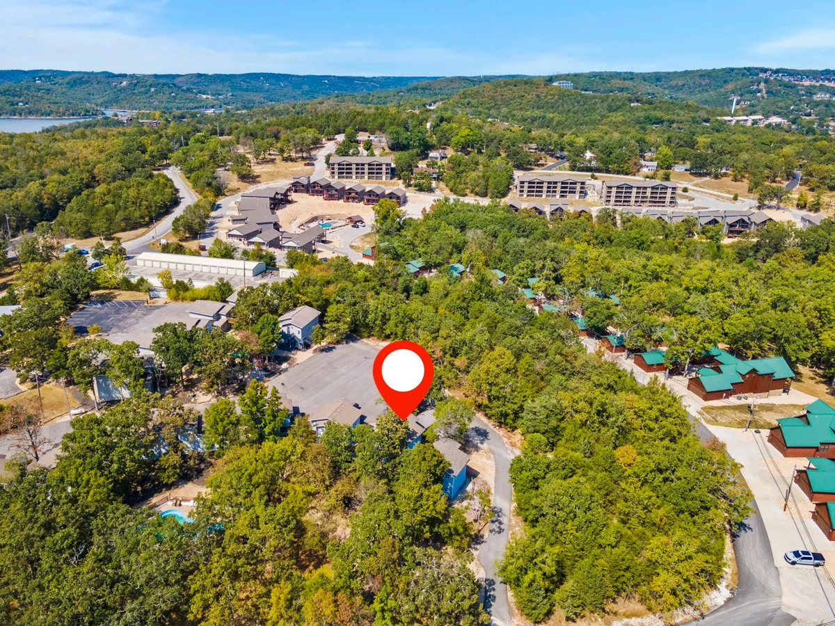 A wide view displays green wooded areas, scattered buildings, a spacious parking area, and the nearby lake, evoking a sense of community and opportunity for group events. People can be seen embarking on nature walks and gathering outdoors, reinforcing the family-friendly and accessible environment.