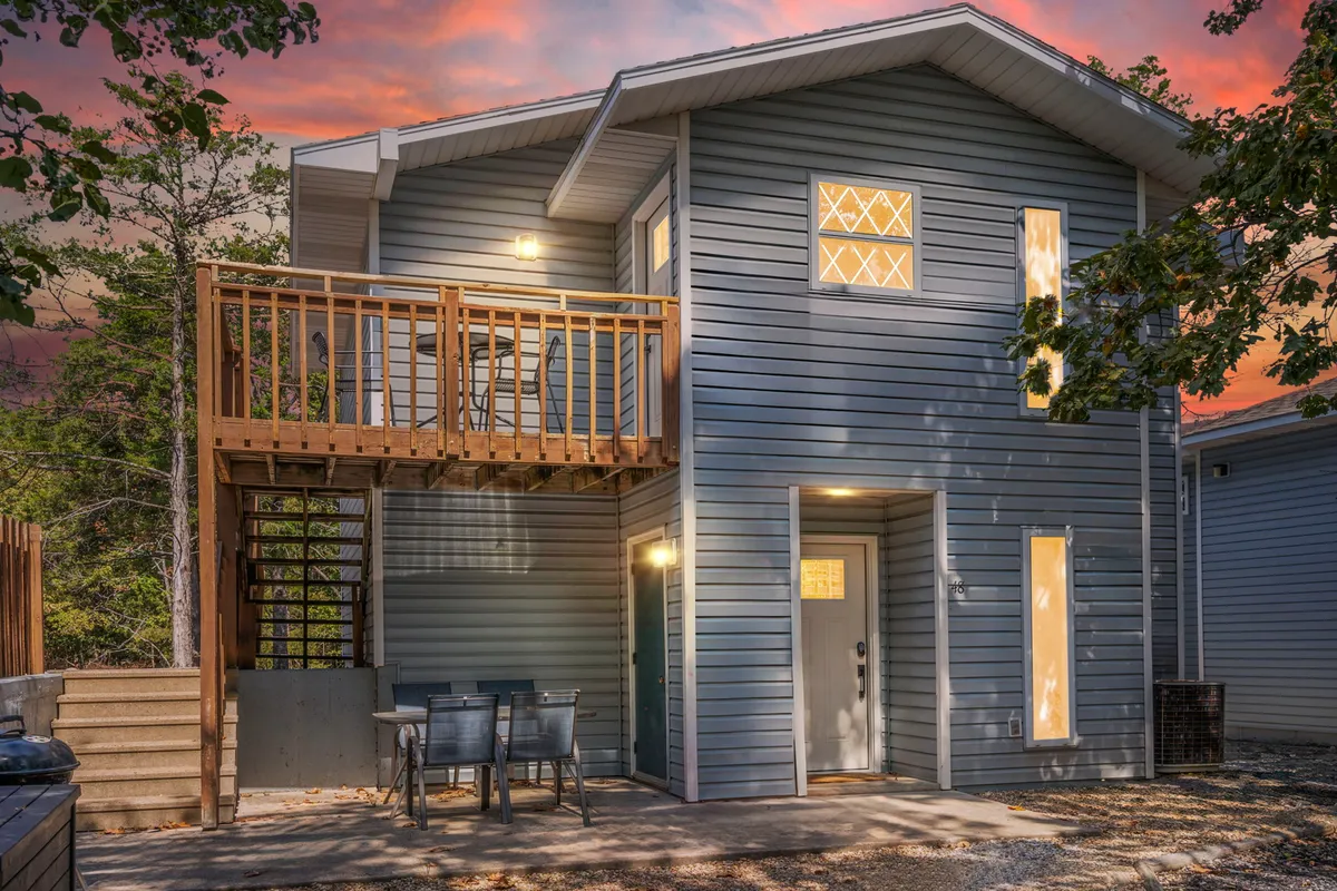 A cozy wooden balcony with outdoor seating, softly illuminated exterior lighting, and wide windows. The inviting setup hints at social moments, sunset views, and a tranquil retreat after outdoor activities.
