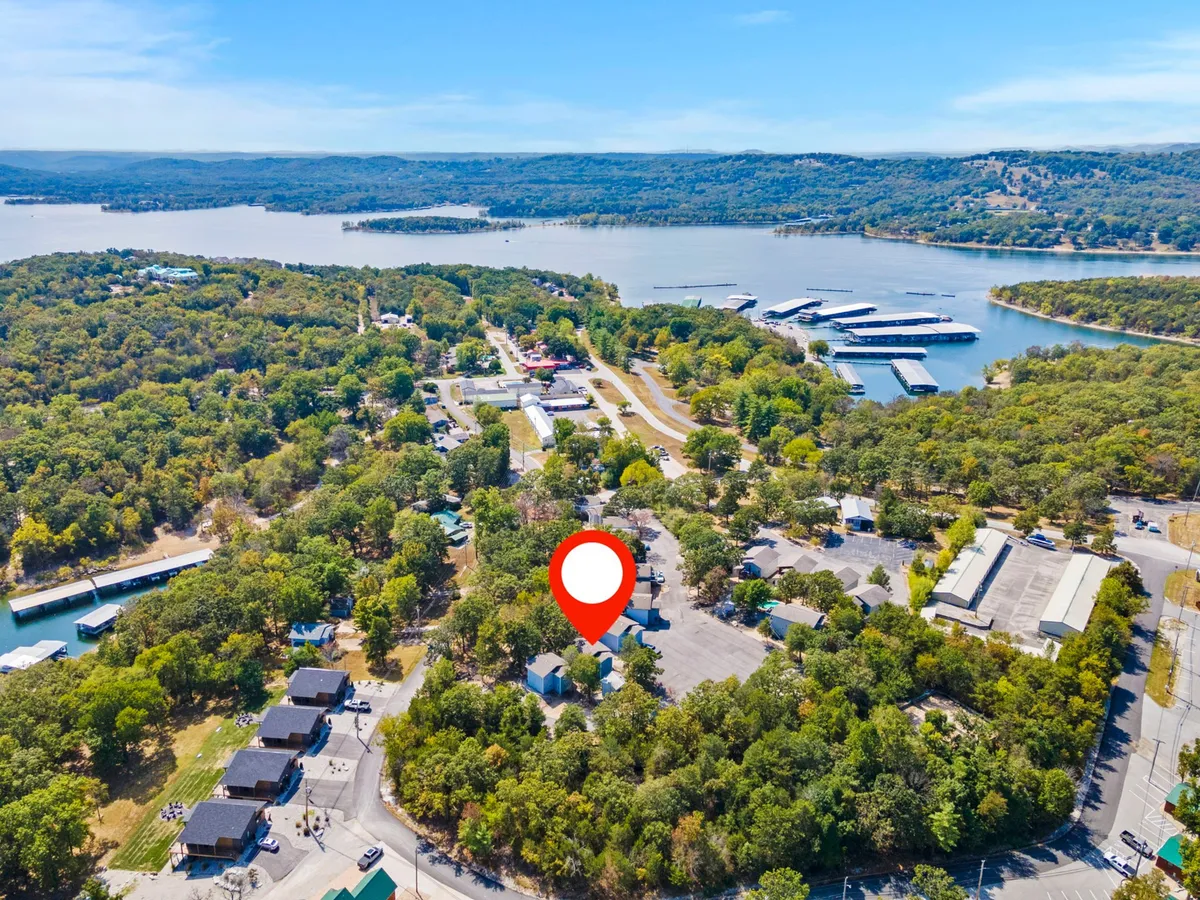 A sweeping exterior view featuring lush greenery, the shimmering expanse of the lake, an active marina, and a cluster of buildings nestled along the shoreline. The scene conveys the vibrant lakeside environment and recreational opportunities available nearby.