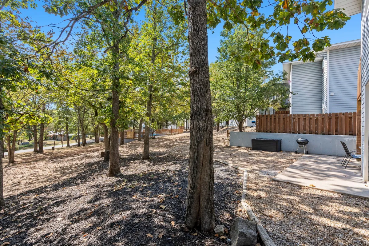 This exterior image shows a tree-shaded patio area equipped for outdoor dining and barbecues, seamlessly blending the comforts of the indoors with fresh Ozarks air. The gravel pathway and tall trees create a relaxing natural setting that invites gatherings and alfresco meals.
